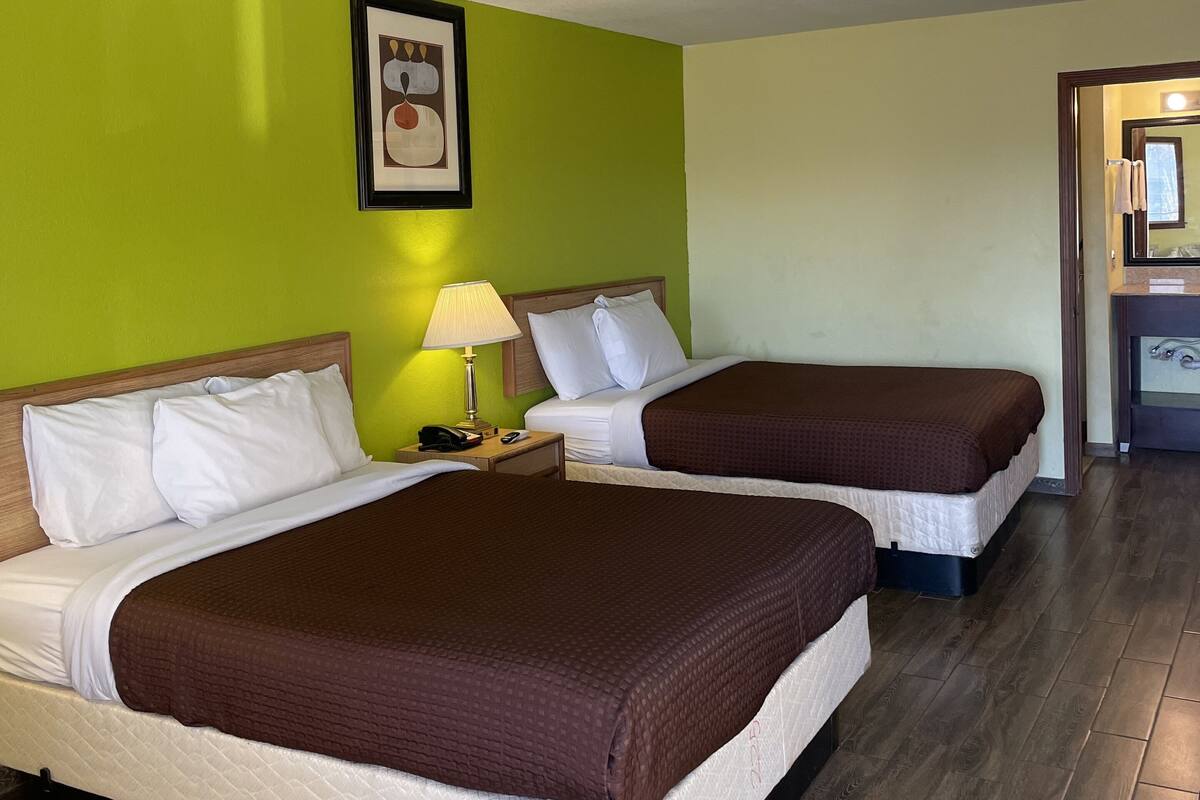 A hotel room with two beds, a nightstand with a lamp, and a framed picture on the wall.