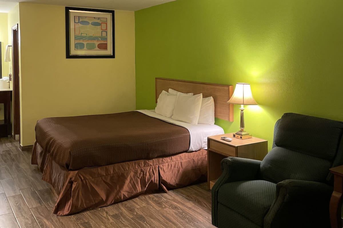 A hotel room with a bed, a chair, a nightstand, and a lamp.