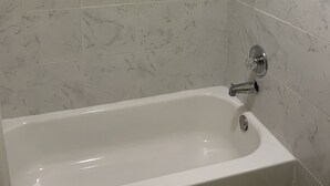 A bathroom with a bathtub, a shower, and marble tiles. - Linder Motor Lodge (Homer)