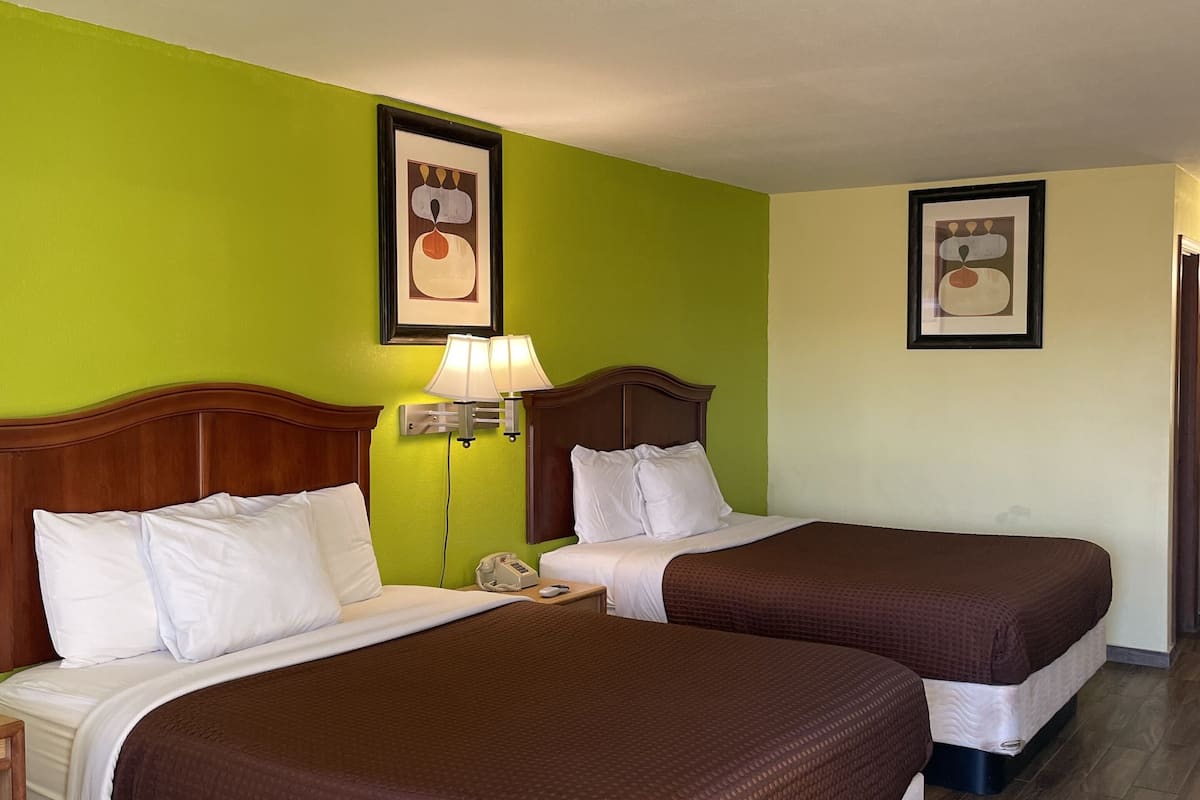 A hotel room with two beds, green walls, wooden headboards, and a framed picture on the wall.