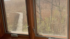 Une fenêtre donnant sur un champ clôturé et des arbres.