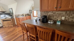 Une cuisine avec des meubles en bois, un grand îlot central doté de tabourets, une machine à café et un dosseret carrelé.
