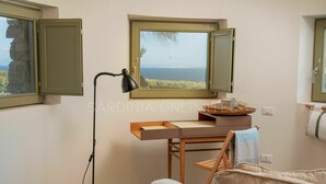Ein Zimmer mit Schreibtisch, Stuhl, Lampe und Meerblick durch ein Fenster.
