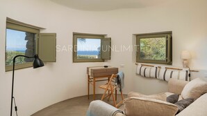 Ein Zimmer mit drei Fenstern, einem Schreibtisch mit Stuhl, einer Lampe und einem Sofa.