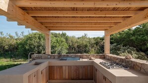 Eine Außenküche mit Steinabdeckplatte, Holzschränken und einem Gasherd.