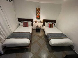 Una habitación con dos camas, cada una con ropa de cama y almohadas estampadas. Entre las camas hay una mesita con una lámpara.