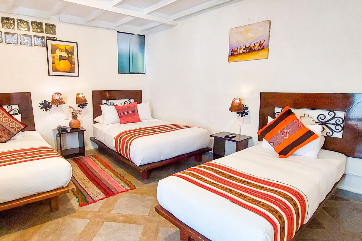 Habitación de hotel con tres camas, cada una con un diseño de cabecera diferente, una mesita y una mesita de noche.