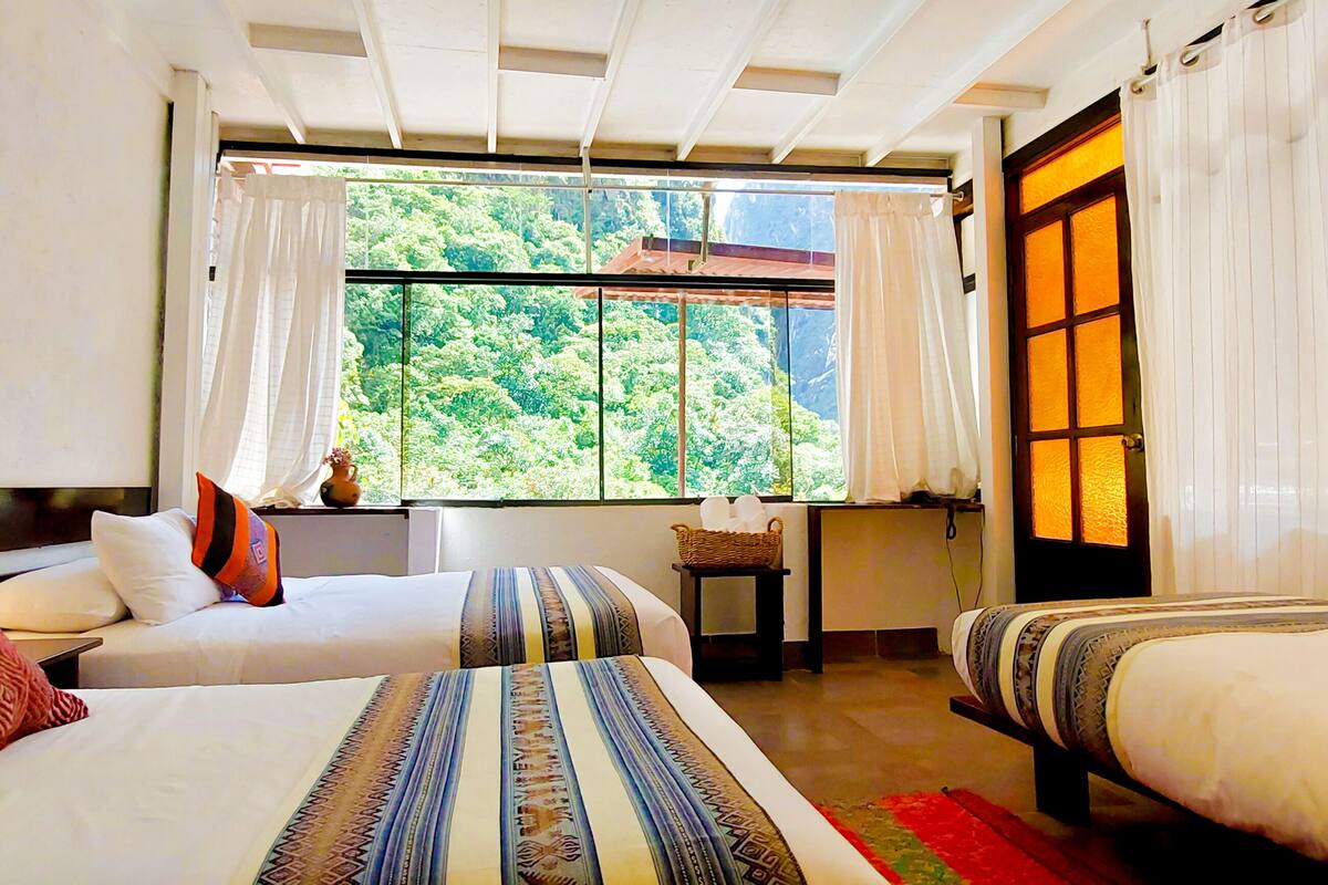 Una habitación de hotel con dos camas, una ventana que da a zonas verdes y una puerta tradicional.