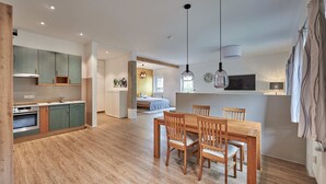 A modern kitchen with wooden cabinets, a dining area with a wooden table and chairs, and a bedroom with a bed and window. - Sicado-Loft vacation apartment 75 sqm, open-plan living room and bedroom, terrace (Aschau im Chiemgau)
