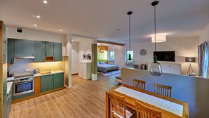 A modern kitchen with a built-in oven, a dining area with a wooden table and chairs, and a bedroom with a bed and a window. - Sicado-Loft vacation apartment 75 sqm, open-plan living room and bedroom, terrace (Aschau im Chiemgau)