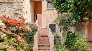 A staircase leading to a building entrance, surrounded by lush greenery and a stone wall.