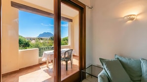 A balcony with a table and chairs, a couch, and a view of greenery and mountains.