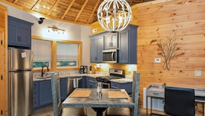 A kitchen with wooden walls, a dining table with chairs, a refrigerator, a microwave, and a chandelier.