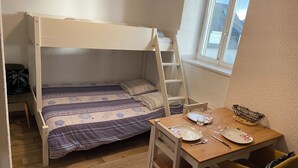 Une petite pièce bien éclairée, avec un lit superposé, une table en bois et une chaise, ainsi qu’une fenêtre donnant sur les montagnes.