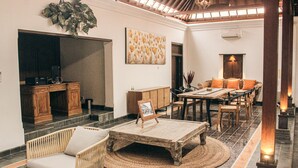 A spacious lobby with a wooden coffee table, wicker sofa, and a dining area with wooden chairs and a table. - Omah Siliran Heritage (Yogyakarta)