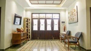 A spacious living area with a wooden bench, a sofa, and a TV mounted on the wall. - Omah Siliran Heritage (Yogyakarta)