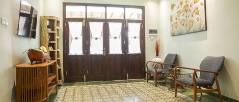 A spacious living area with a large wooden door, a television mounted on the wall, and a patterned floor.