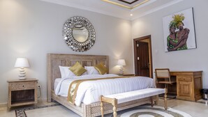 A bedroom with a bed, two bedside tables with lamps, a wooden bench, a decorative mirror, a wooden door, and a painting on the wall. - Omah Siliran Heritage (Yogyakarta)