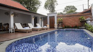 A swimming pool with blue mosaic tiles, surrounded by lounge chairs and a small table. - Omah Siliran Heritage (Yogyakarta)