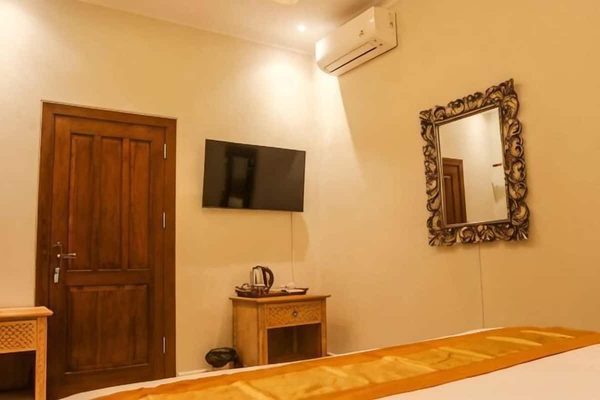 A hotel room with a wooden door, a television, a mirror, and a small table with a kettle.