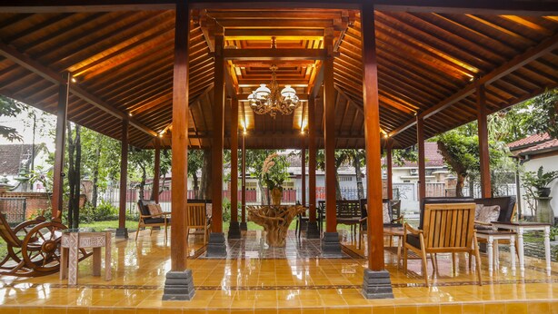 A covered outdoor seating area with wooden furniture and a tiled floor. - Omah Siliran Heritage (Yogyakarta)