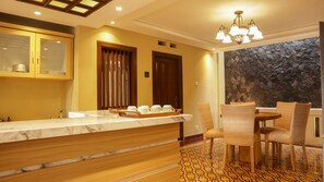A modern kitchen with a marble countertop, wooden cabinets, and a dining area with wicker chairs and a patterned floor. - Omah Siliran Heritage (Yogyakarta)