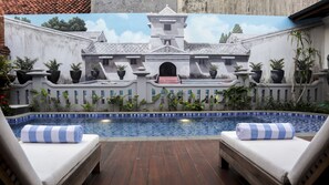 A pool area with two lounge chairs, a tiled pool, and a mural of a colonial-style building. - Omah Siliran Heritage (Yogyakarta)