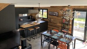 Una cocina moderna con una pared decorativa de madera, un comedor con mesa de vidrio y un amplio ventanal con vistas al exterior.
