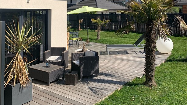 Un patio moderno al aire libre con mobiliario de mimbre, una palmera y vistas a montañas nevadas.