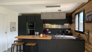 Una cocina moderna con una isla central, armarios negros, electrodomésticos de acero inoxidable y una pared de acento de madera.