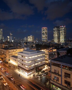 Un paisaje urbano nocturno con edificios modernos, una calle concurrida y ventanas iluminadas.