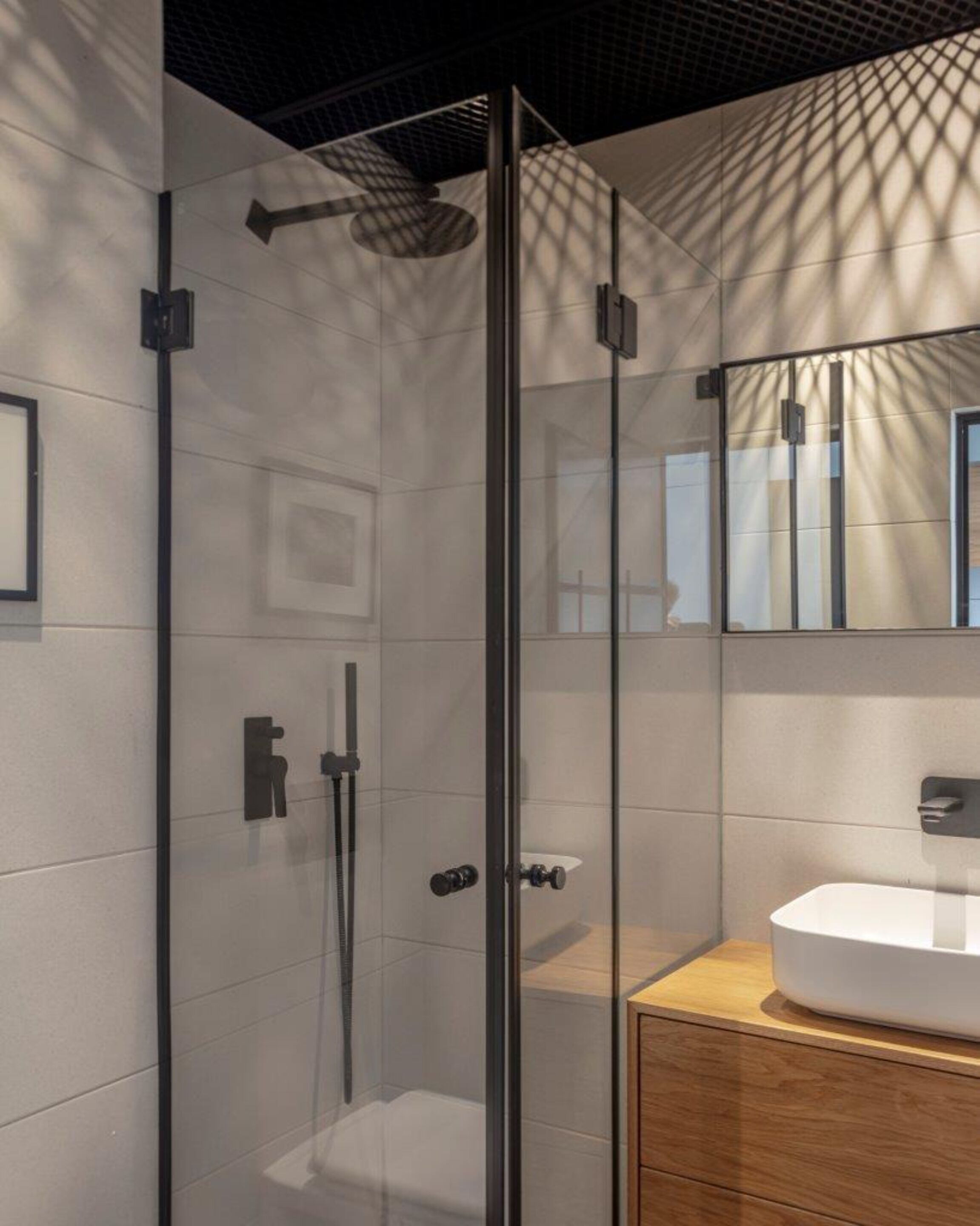 Un baño moderno con ducha envuelta en vidrio, un lavamanos blanco y un mueble de madera.