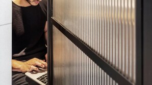 A person using a laptop in a room with a modern design, featuring a glass partition and a framed picture on the wall. - DeBlox living - Ben Avigdor (Tel Aviv)