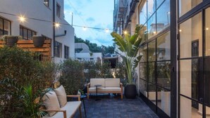 A modern outdoor patio with a sofa and chairs, surrounded by potted plants and a stone floor. - DeBlox living - Ben Avigdor (Tel Aviv)