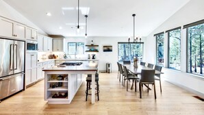 Cocina moderna con una isla central, electrodomésticos de acero inoxidable y amplias ventanas con vistas a árboles.