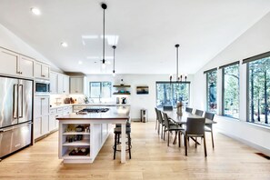 A modern kitchen with a central island, stainless steel appliances, and large windows offering a view of trees.