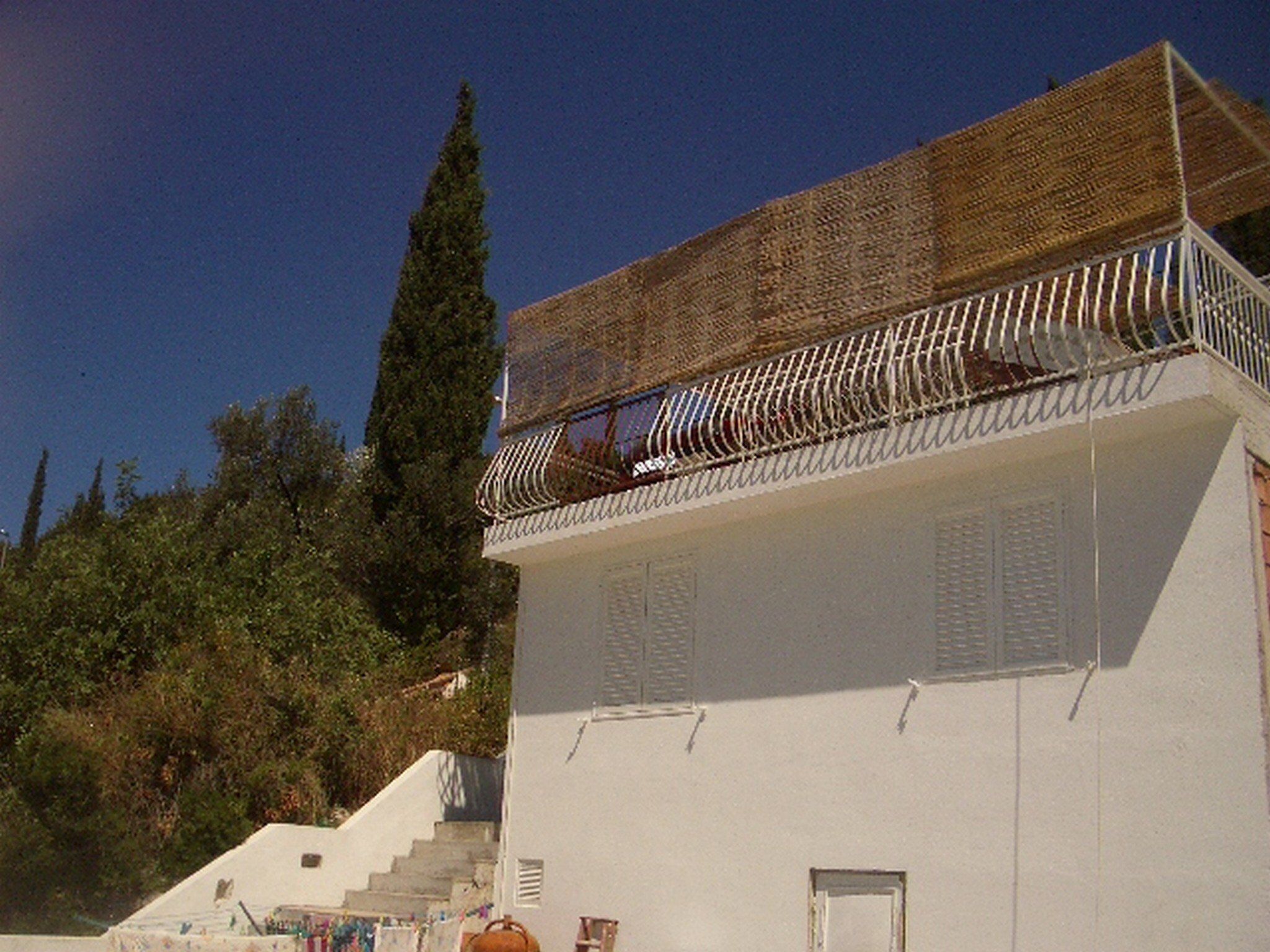 Ein Gebäude mit weißer Fassade, einem hölzernen Balkon und einer Treppe zum Eingang.