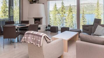 A modern living room with a fireplace, comfortable seating, and large windows offering a view of trees and a body of water.