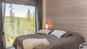 Un dormitorio con una cama grande, una mesita de noche y vistas a árboles a través de una ventana.