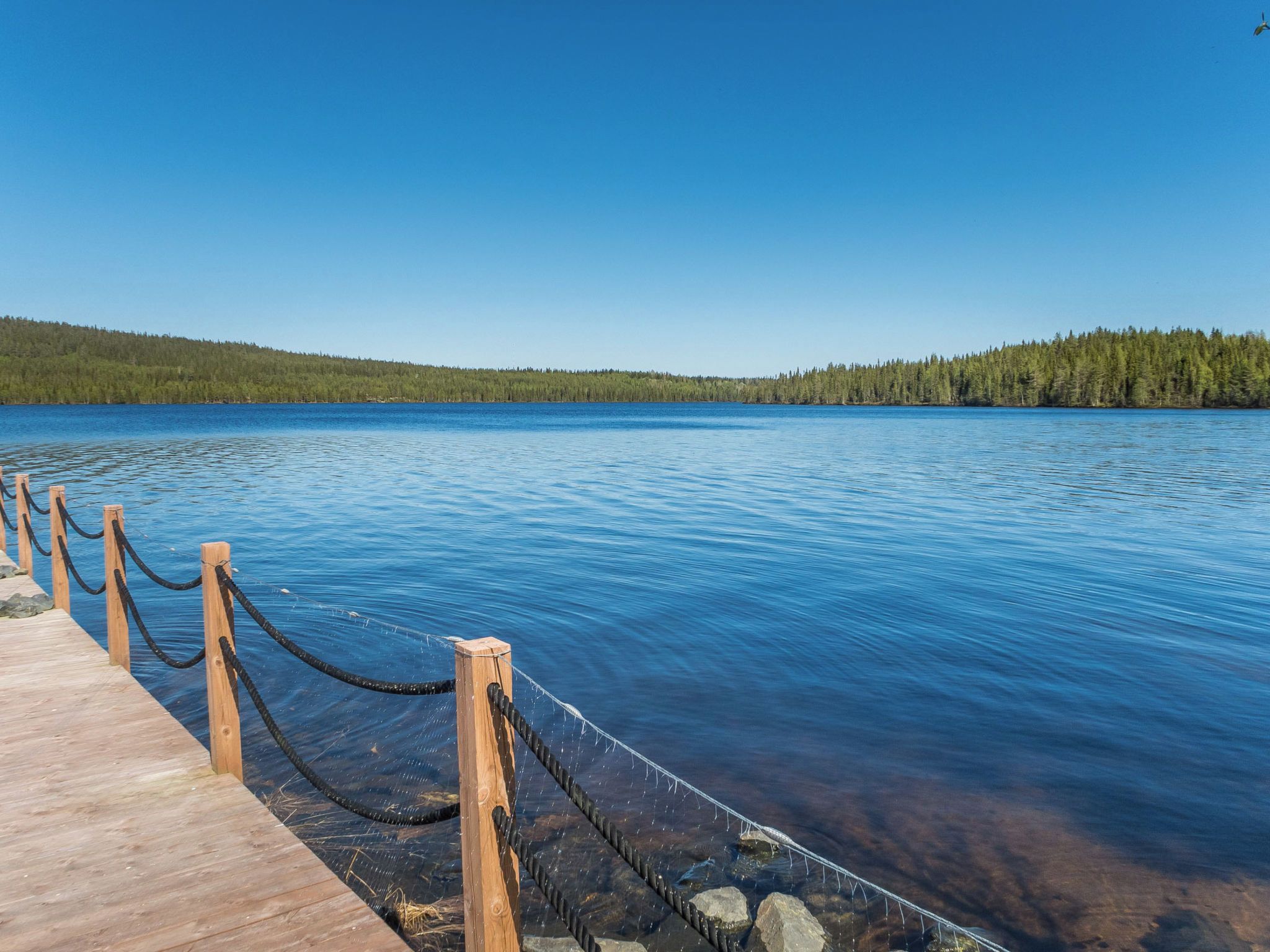 Une jetée en bois s’étendant sur un lac paisible, sous un ciel dégagé.
