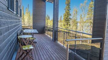 A wooden deck with a table and chairs, overlooking a forested area.
