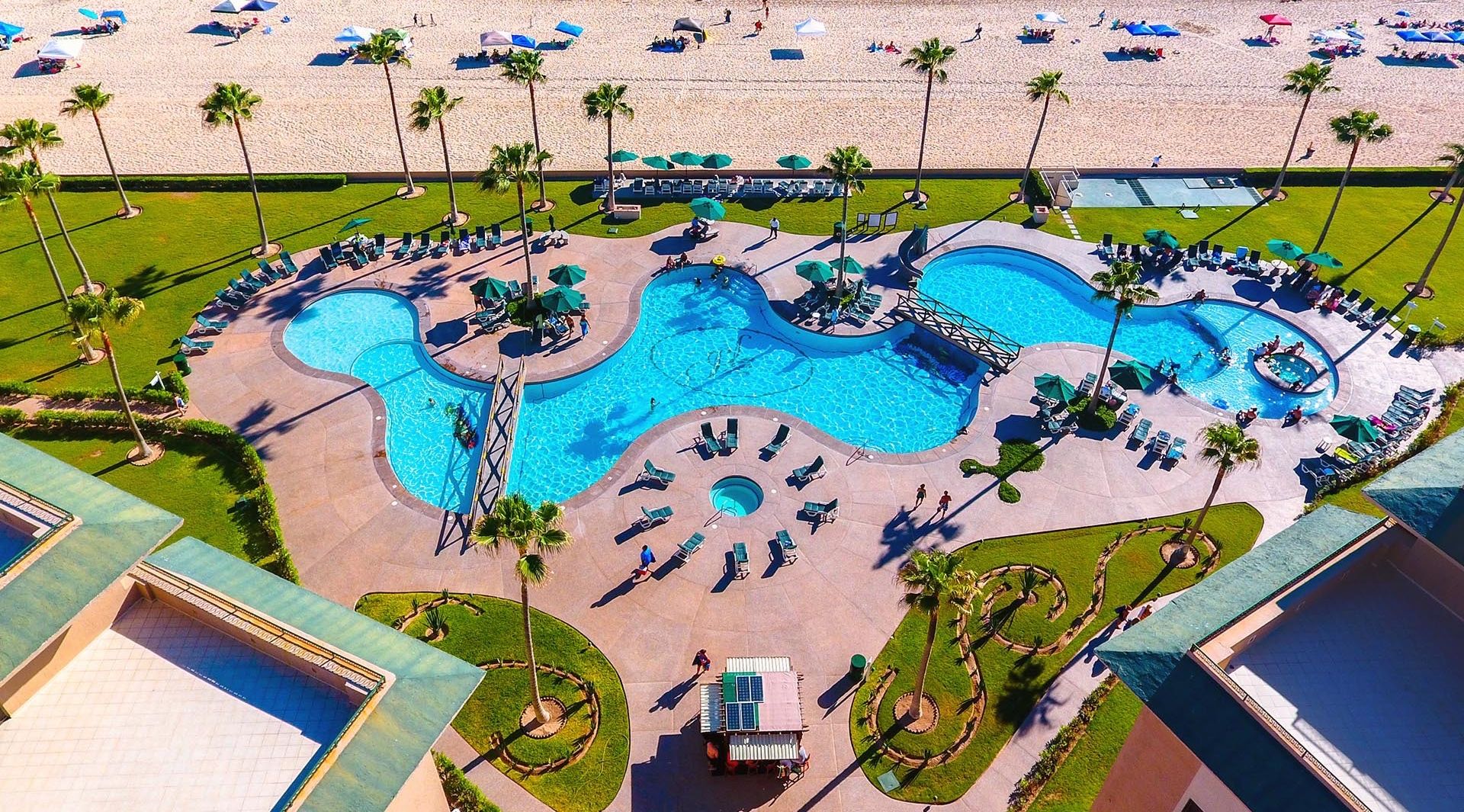 Ein Resort mit großem Poolbereich, Zugang zum Strand und Palmen.