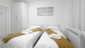 Habitación de hotel con dos camas, ropa de cama blanca, una manta marrón, un cuadro en la pared y un radiador blanco.