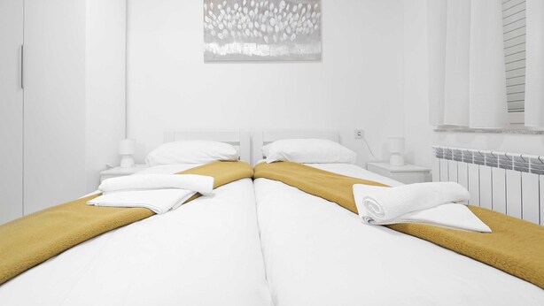Una habitación de hotel moderna con una cama grande, ropa de cama blanca, una manta color mostaza y una obra de arte colgada en la pared.