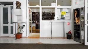 Un área de recepción con mostrador, una planta en maceta, un busto de escultura y una estantería llena de libros.
