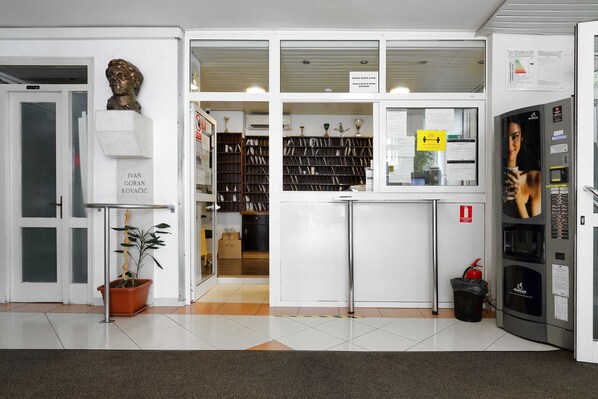 A reception area with a reception desk, a potted plant, a bust sculpture, and a bookshelf filled with books.
