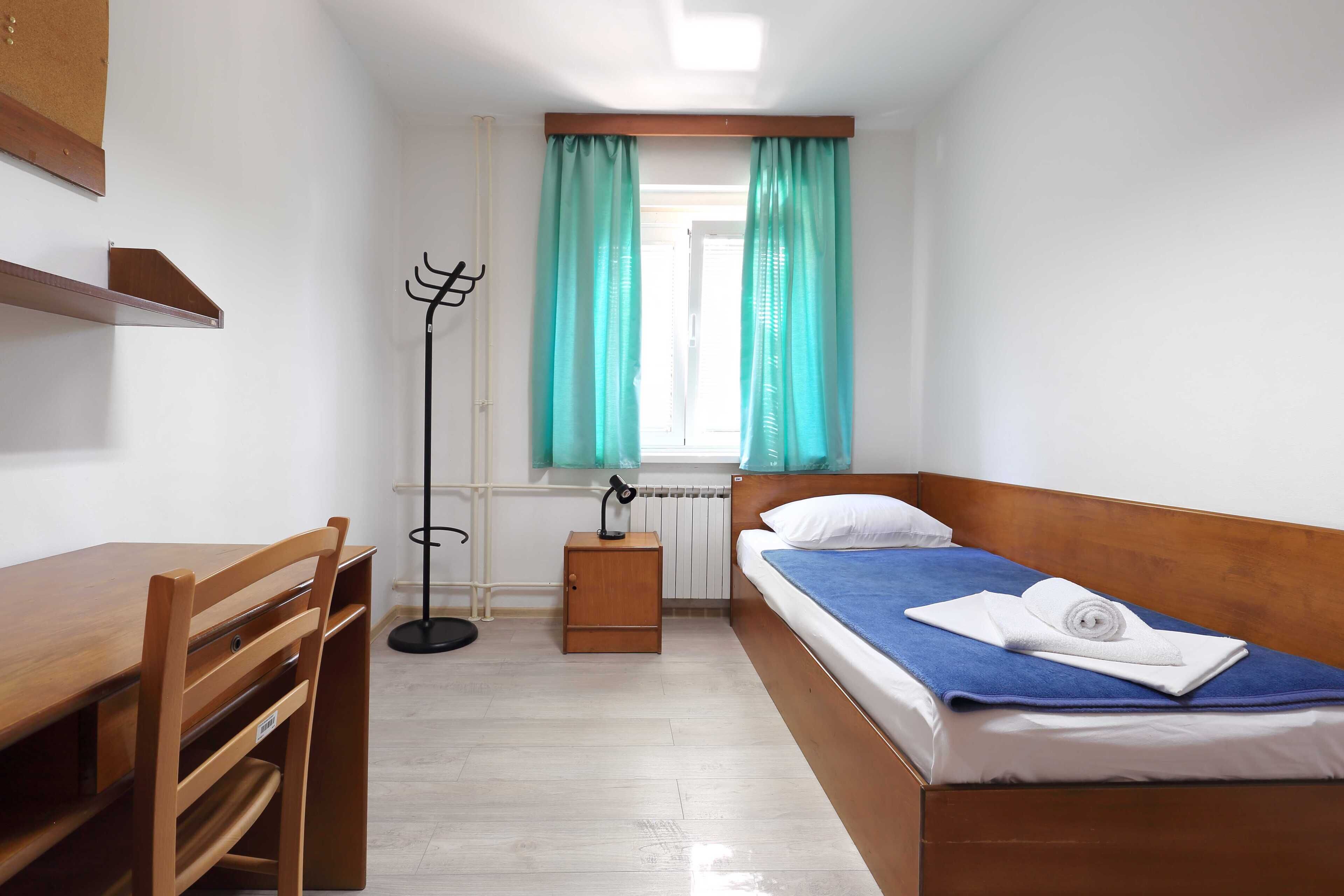 Una habitación pequeña con una cama de madera, un escritorio y una silla.