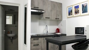 Una cocina compacta con un fregadero, estufa y microondas. Hay armarios y una pequeña mesa.
