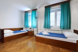 A room with two wooden beds, a radiator, a floor lamp, and teal curtains. - Student Dormitory Rooms Ivan Goran Kovacic (Rijeka)