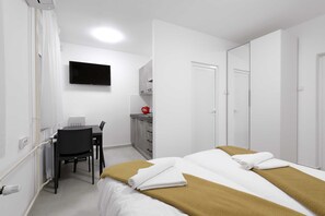 A hotel room with a bed, a desk, a chair, a TV, and a wardrobe.